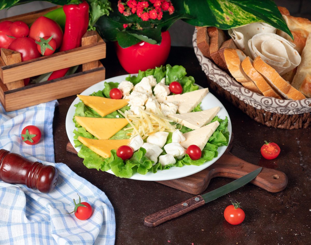 Plate of sliced cheeses on salad with cherry tomatoes and bread