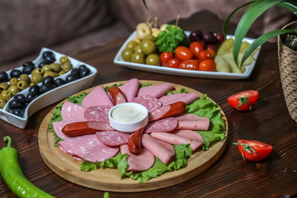 Plate of mortadella and sausages surrounded by olives and fresh vegetables