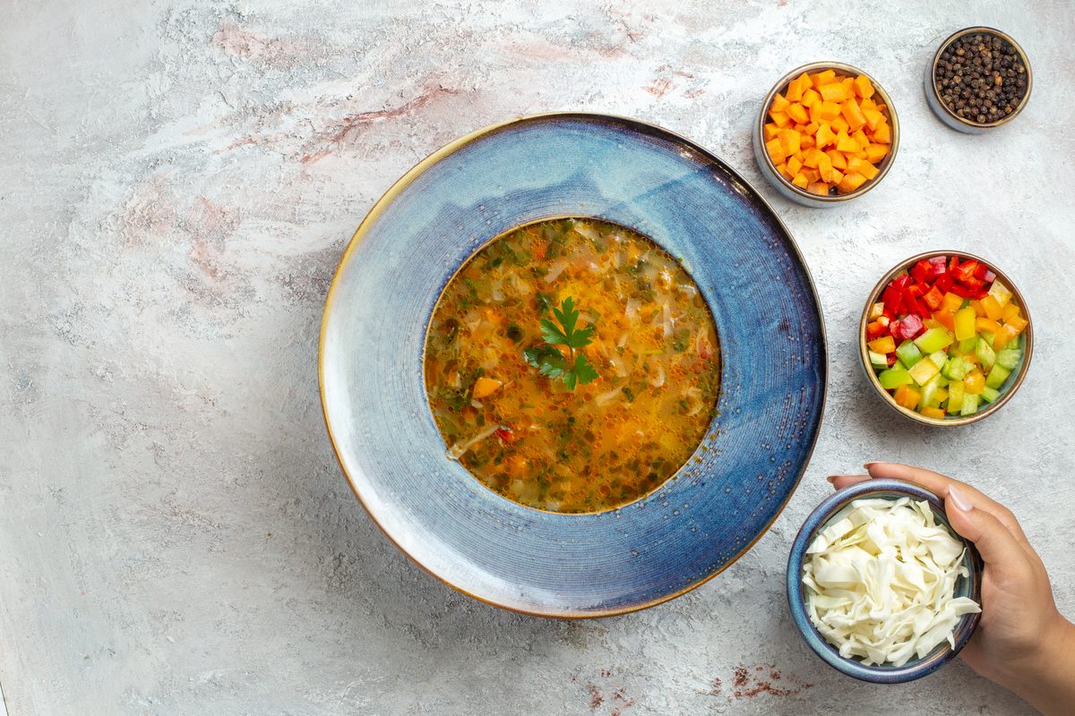 Assiette de soupe de légumes entourée de petits bols de légumes coupés