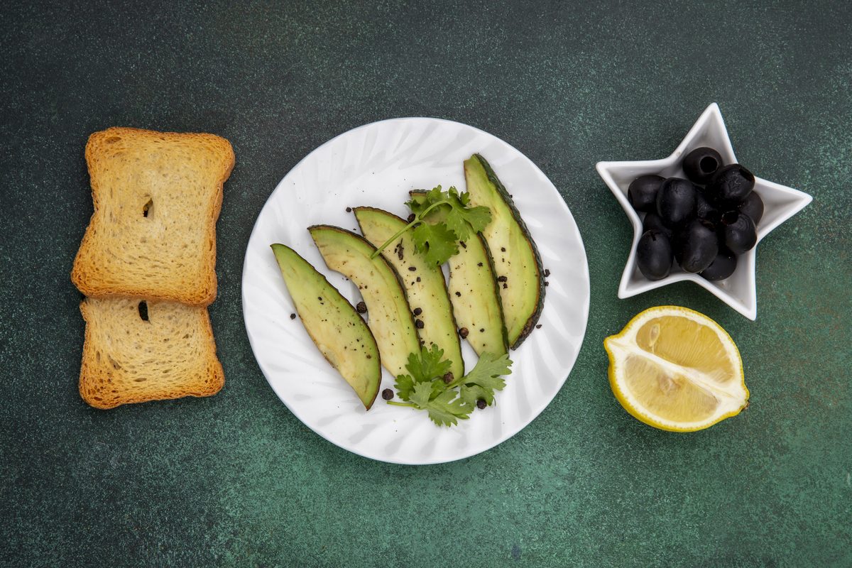 Plate of avocado slices with black olives, lemon and toasted bread