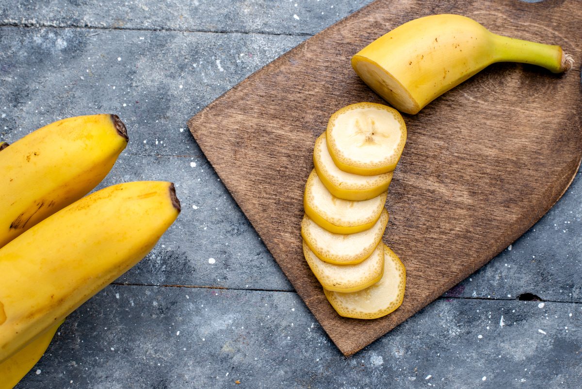 Banana cut into slices on a board next to whole bananas