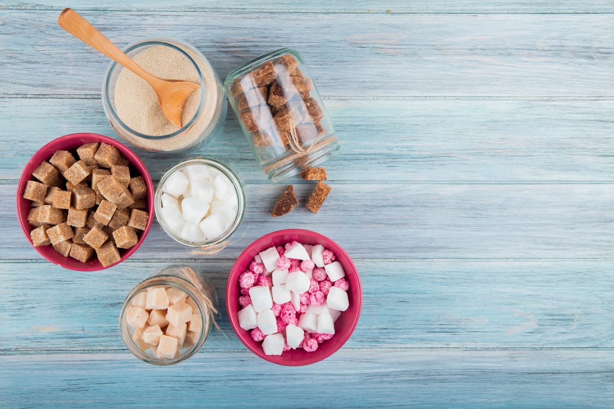 Jars and bowls of white sugar, brown sugar and marshmallows on a blue table