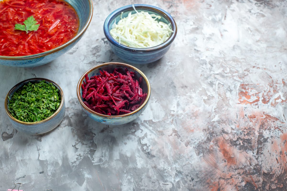 Bowl of beetroot borscht surrounded by grated cabbage, parsley and raw beetroot