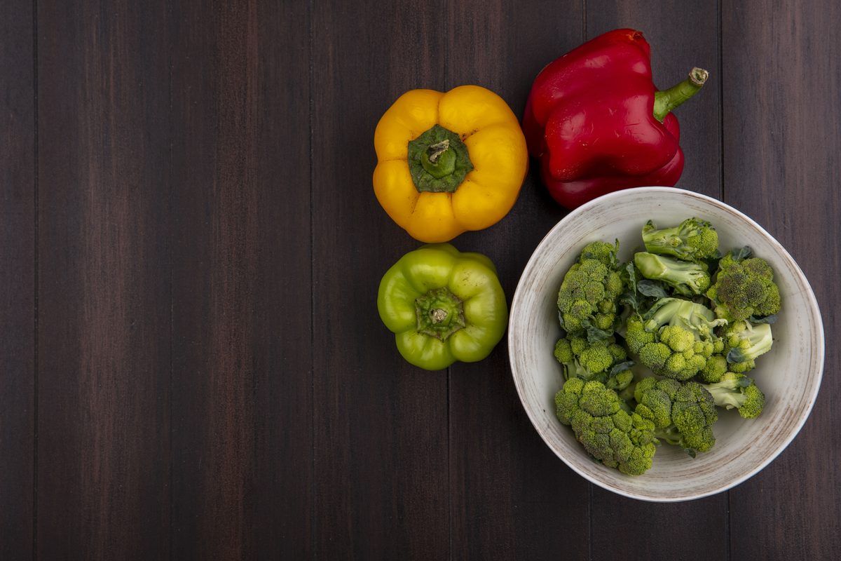 Bol de brocoli et poivrons jaune, rouge et vert sur une table en bois sombre