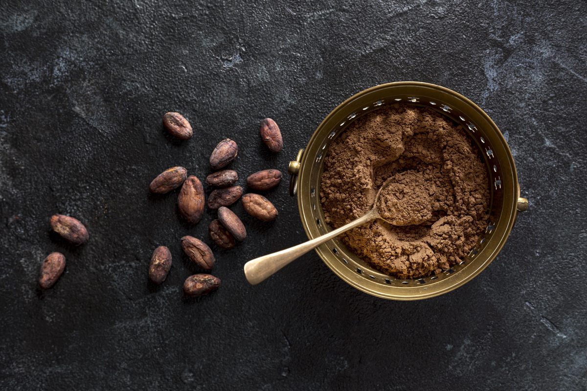 Bowl of cocoa powder and cocoa beans on a black background