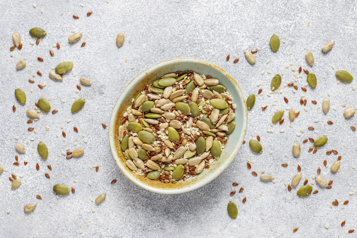 Bowl of pumpkin, sunflower and flax seeds on a light grey background