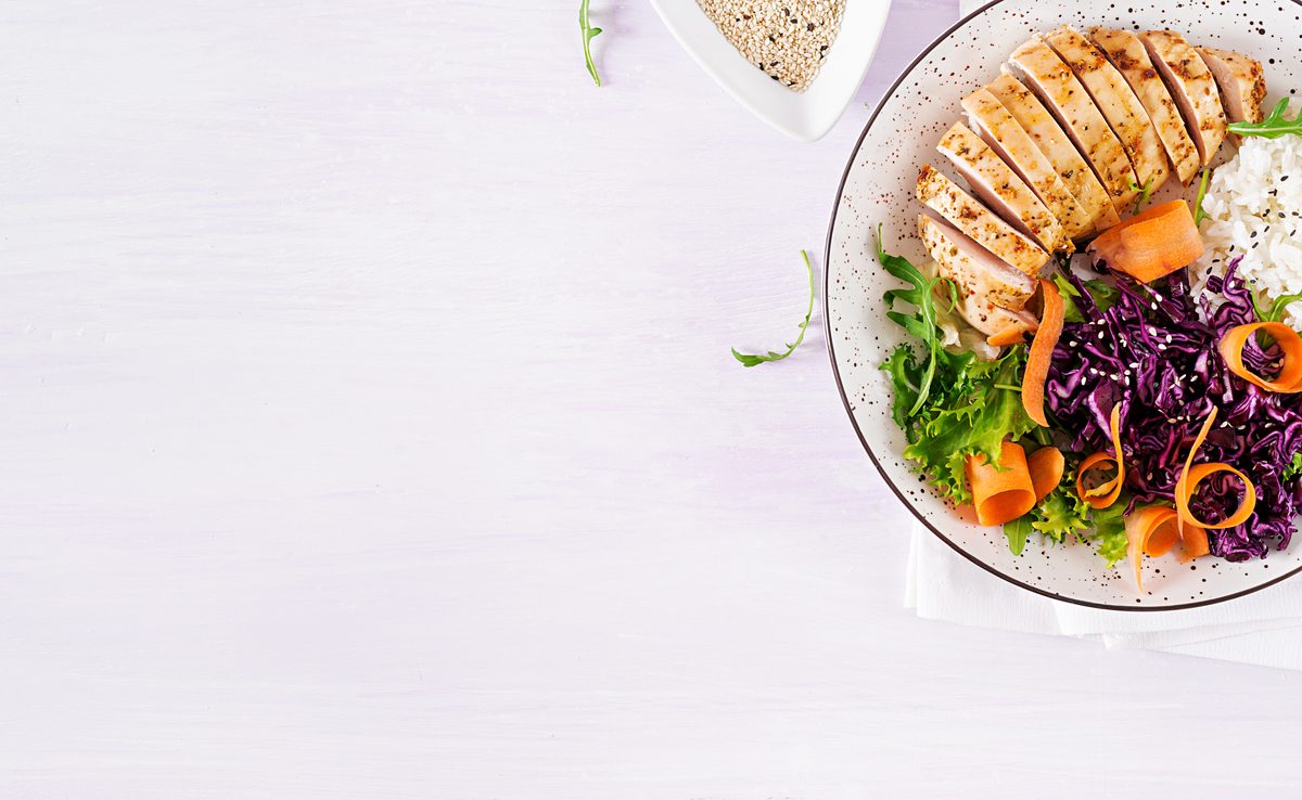 Bowl of grilled chicken, rice, red cabbage, carrots and salad