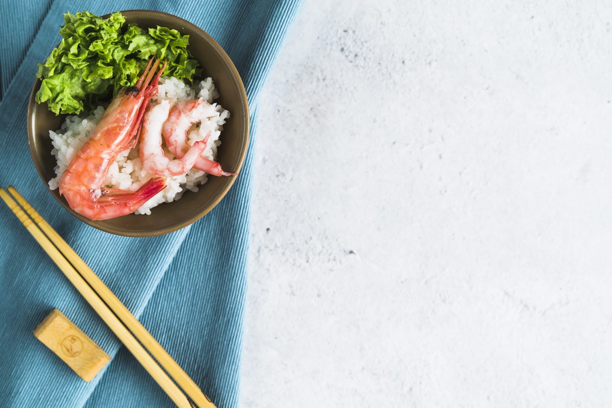 Rice bowl topped with prawns and salad with chopsticks