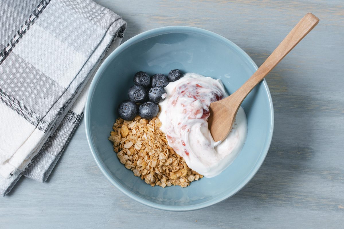 Bowl of plain yoghurt, oat flakes and blueberries with a wooden spoon