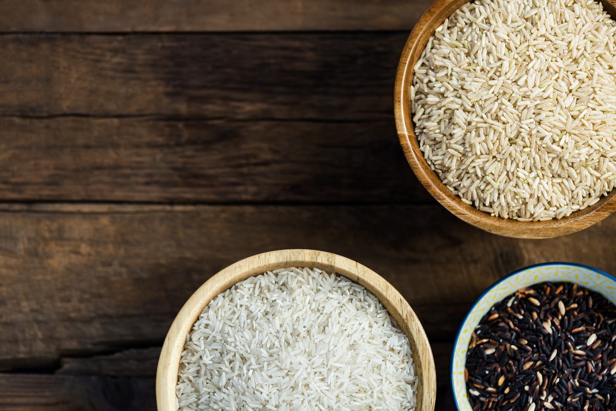 Bowls of brown rice, white rice and black rice on a wooden table