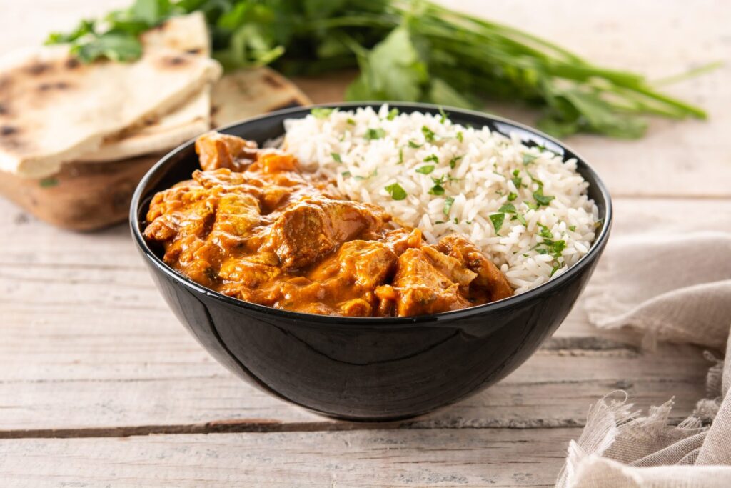 Butter chicken in a black bowl on a wooden table