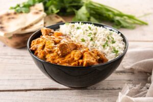 Butter chicken in a black bowl on a wooden table
