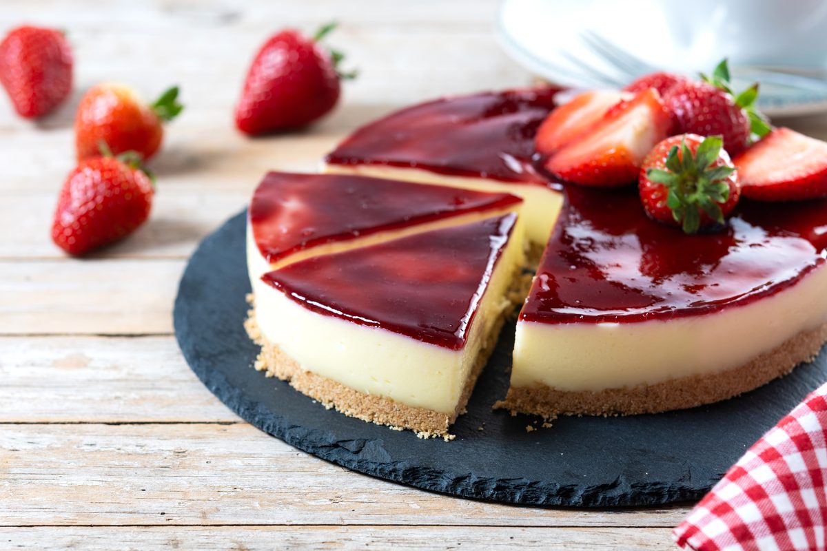 Cheesecake topped with strawberry coulis on a slate board with fresh strawberries