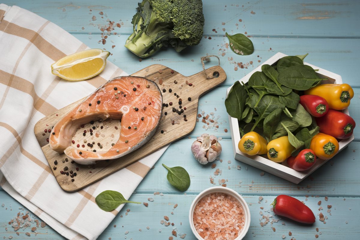 Darne de saumon cru sur une planche avec épinards, poivrons et brocoli