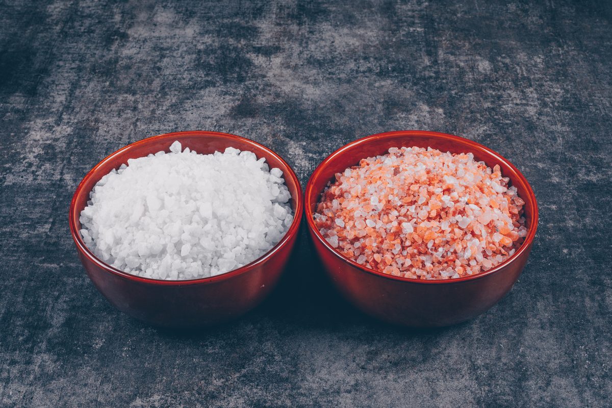 Two bowls of salt, white coarse salt and pink salt, on a dark background