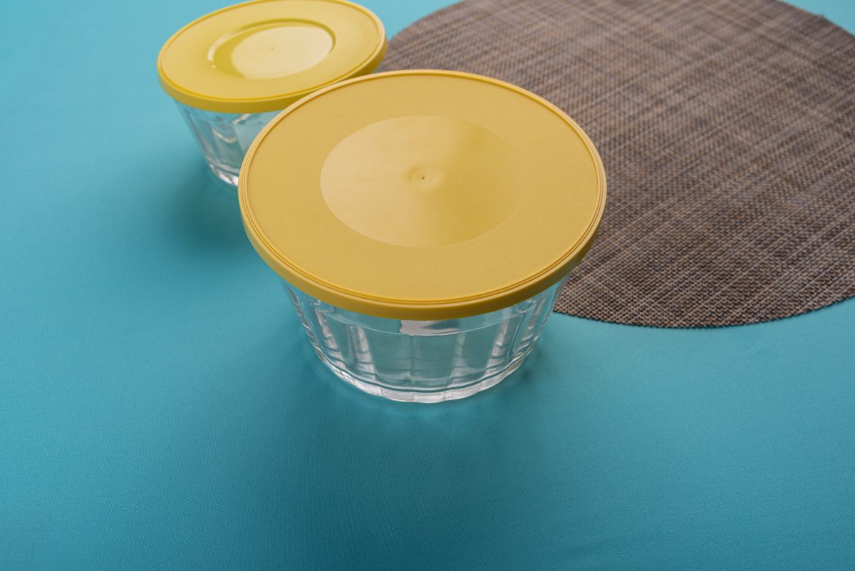 Two glass bowls with yellow lids on a blue background