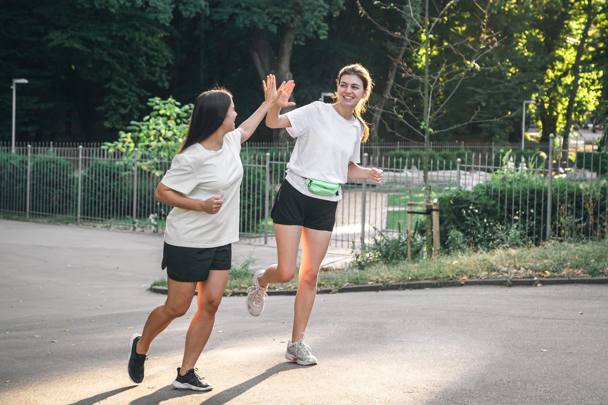 Deux jeunes femmes courant et se tapant dans la main dans un parc