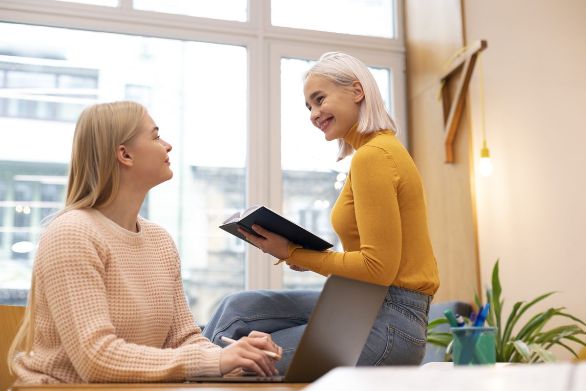 Two young women revising with a computer and a notebook