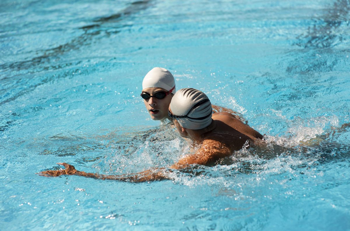 Two swimmers in swimming caps swimming in a pool