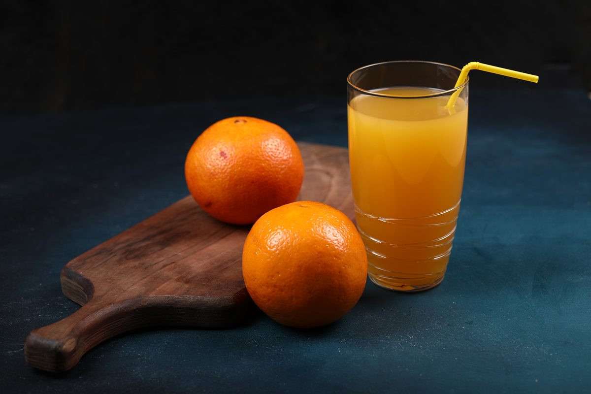 Two whole oranges on a board next to a glass of orange juice