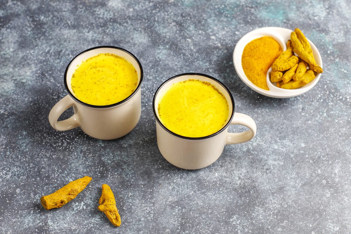 Two cups of golden turmeric milk next to dried roots