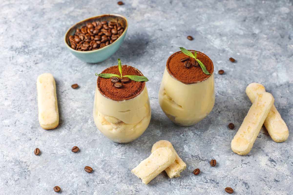 Two glasses of tiramisu dusted with cocoa and surrounded by coffee beans