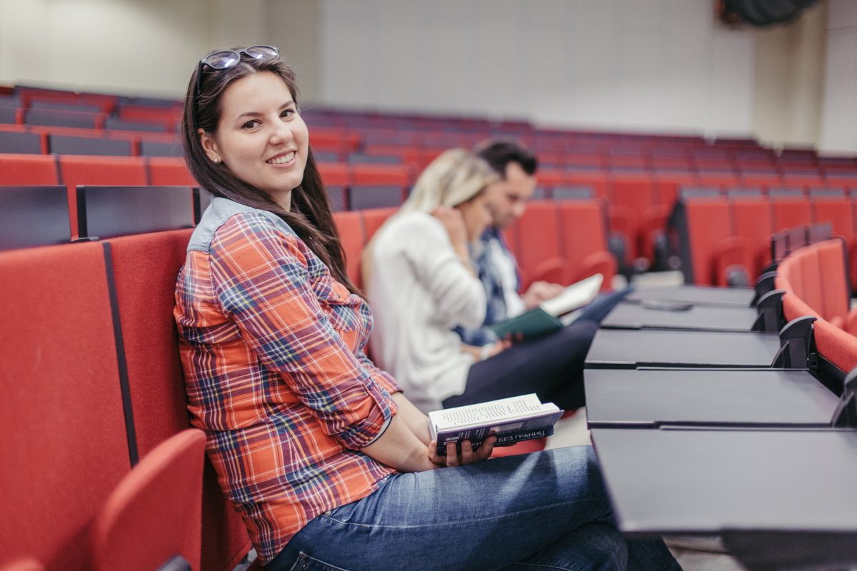 Smiling student sitting with a book in a lecture theatre