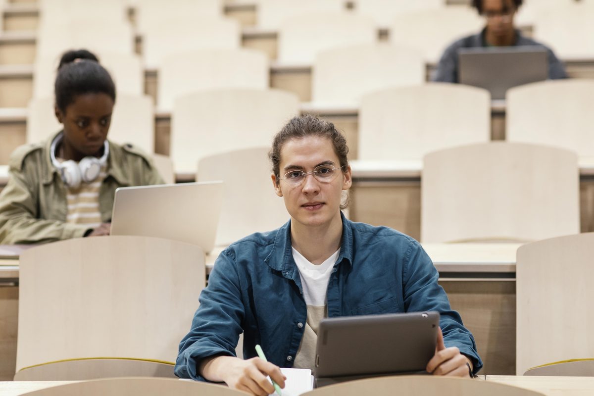 Étudiants assis dans un amphithéâtre avec tablette et ordinateur