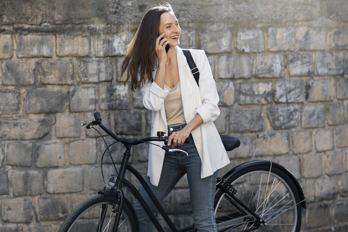 Woman on the phone holding her bike in front of a stone wall
