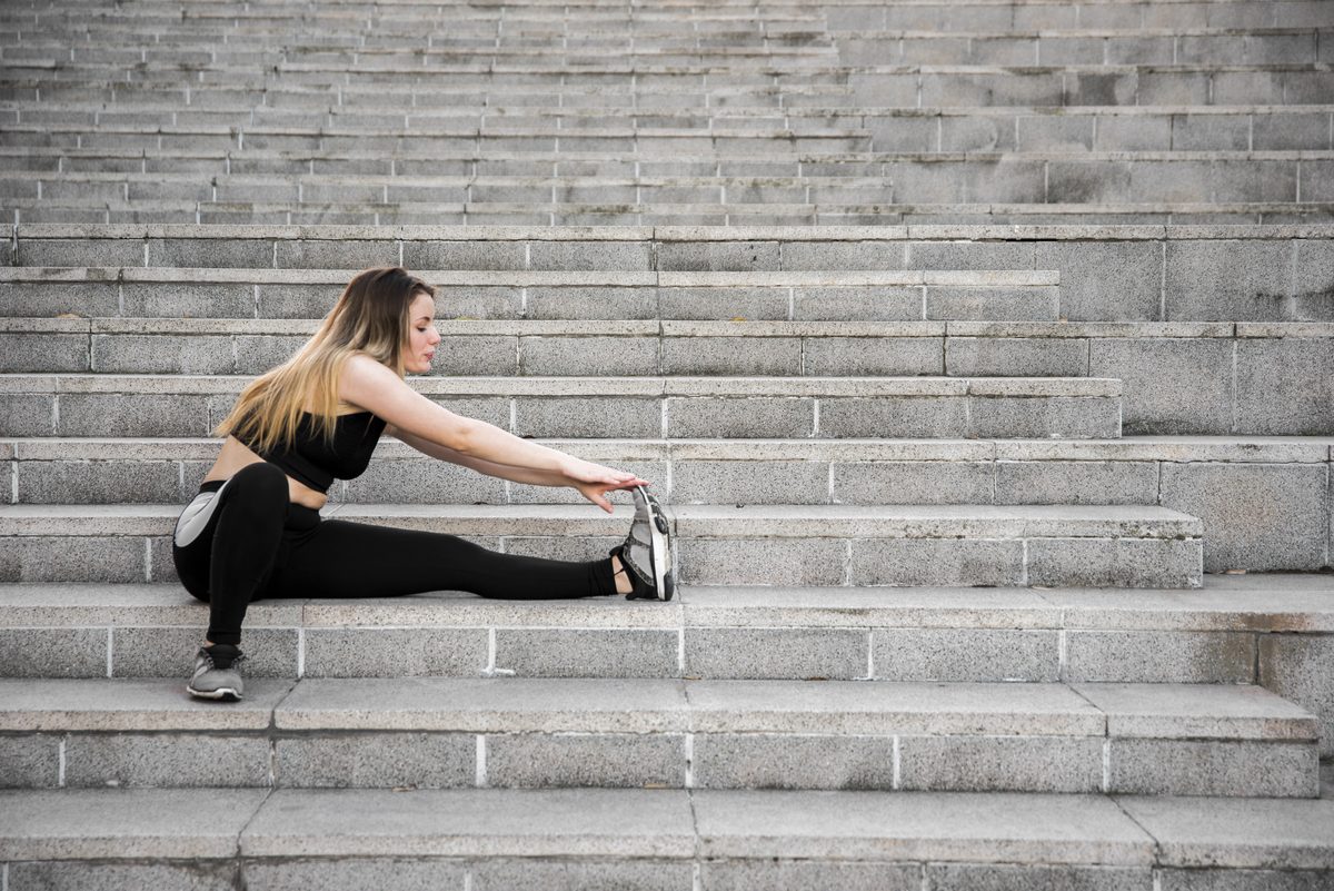 Woman stretching her legs while sitting on stone steps