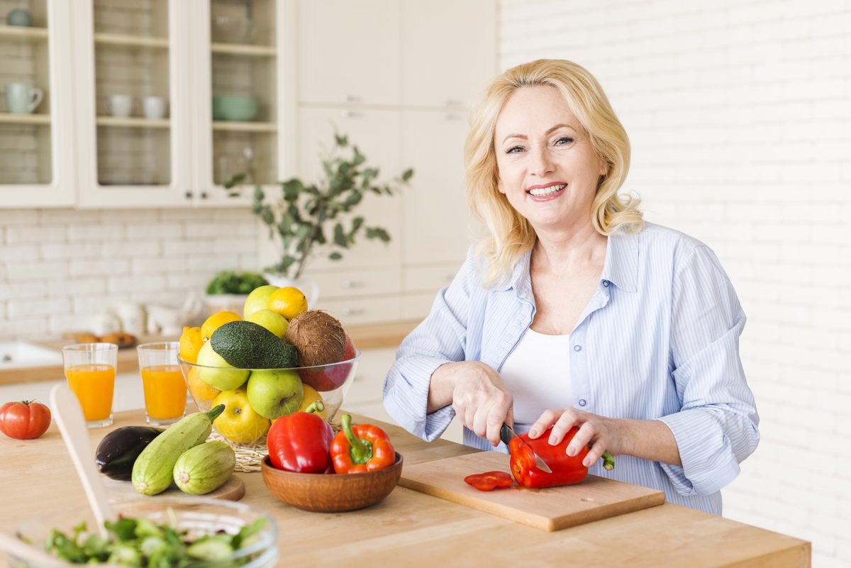 Femme souriante coupant un poivron rouge dans une cuisine lumineuse