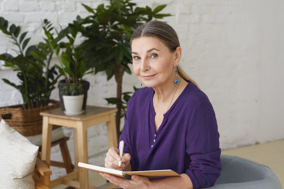 Femme souriante prenant des notes dans un carnet, entourée de plantes
