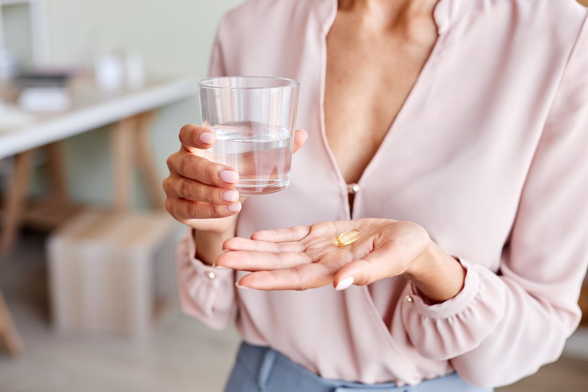 Probiotic capsule held between two fingers next to a glass of water