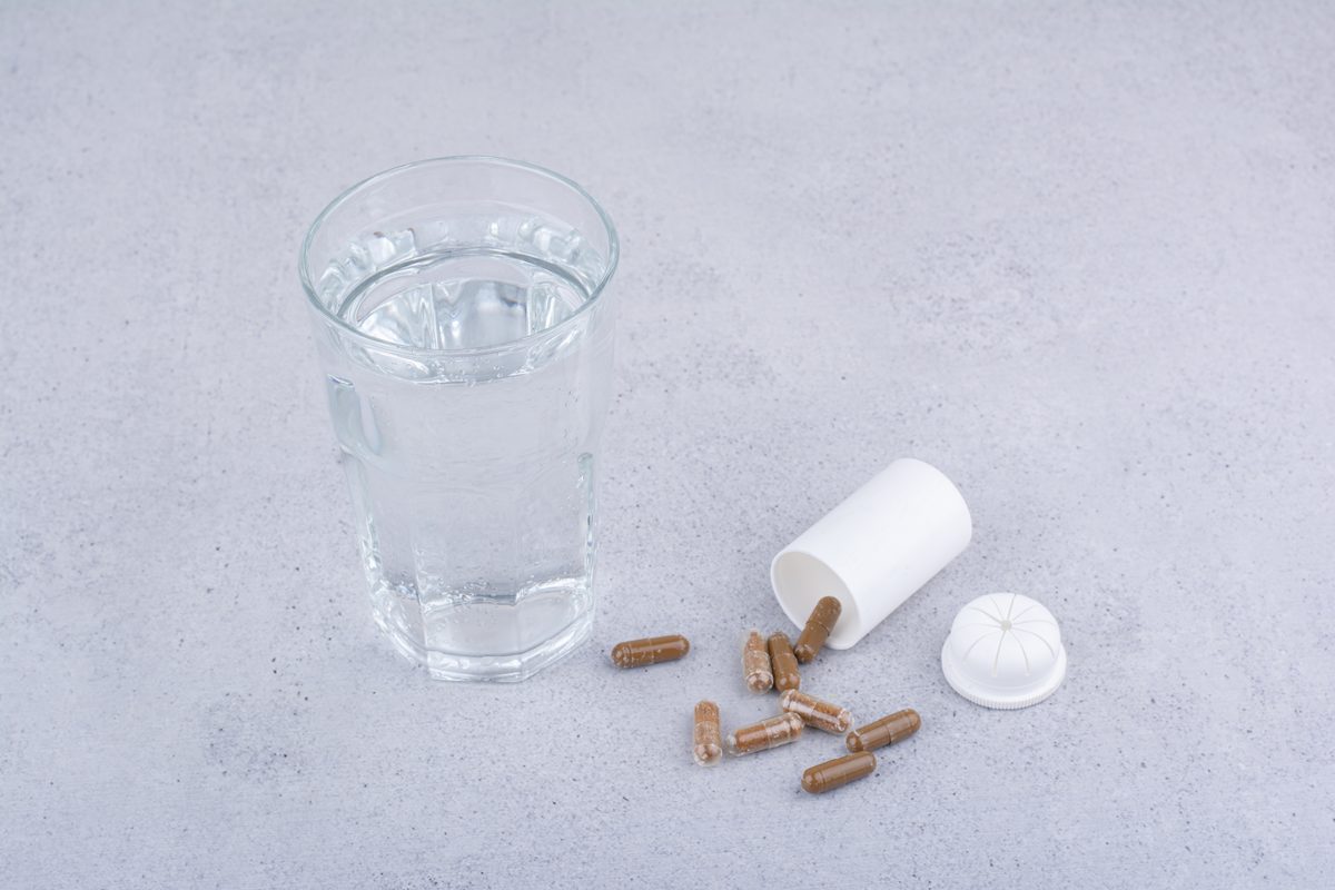 Gélules et verre d'eau posés sur une table grise