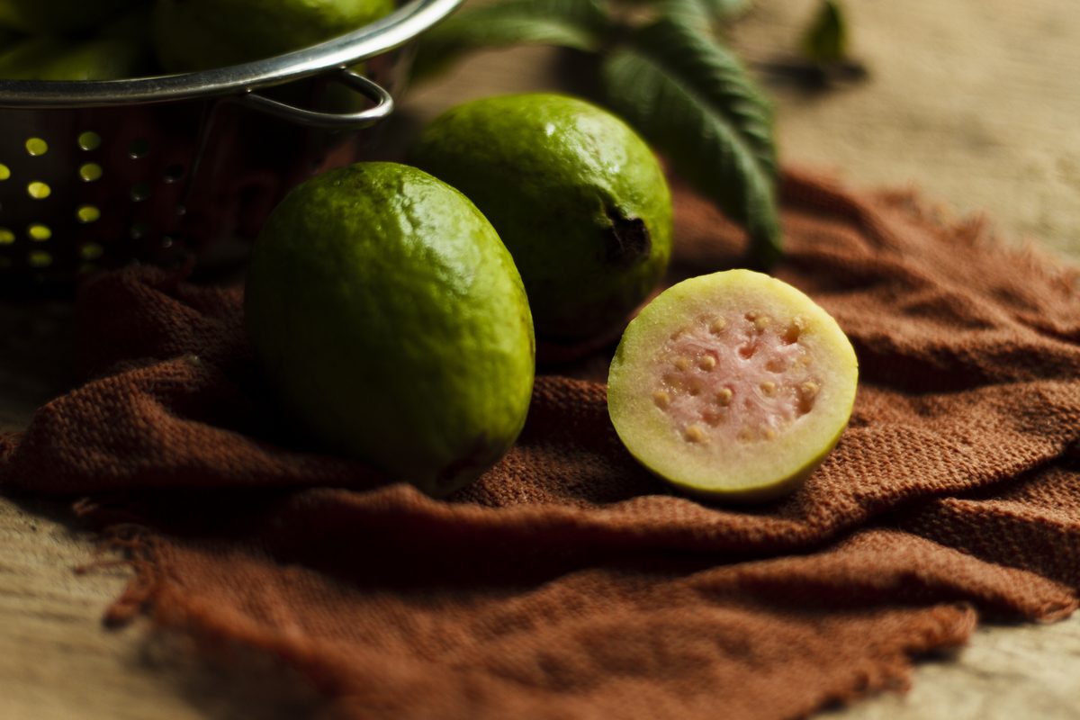 Whole green guavas and one pink-fleshed half on a cloth