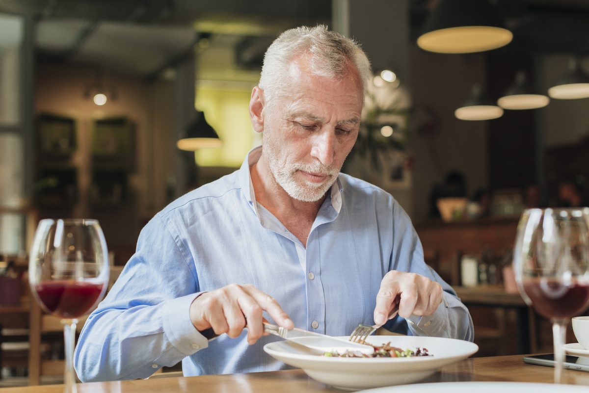 Homme âgé aux cheveux blancs attablé devant son assiette au restaurant