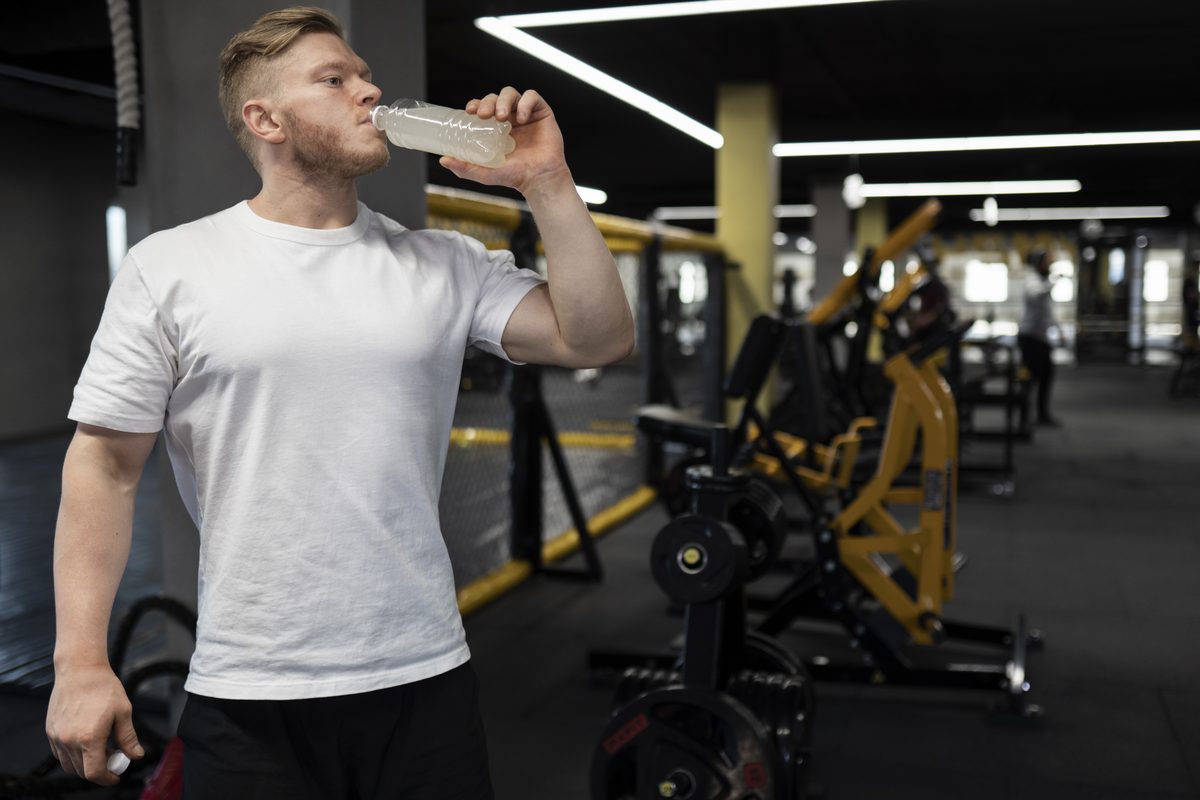 Homme en tee-shirt blanc buvant dans une bouteille en salle de sport