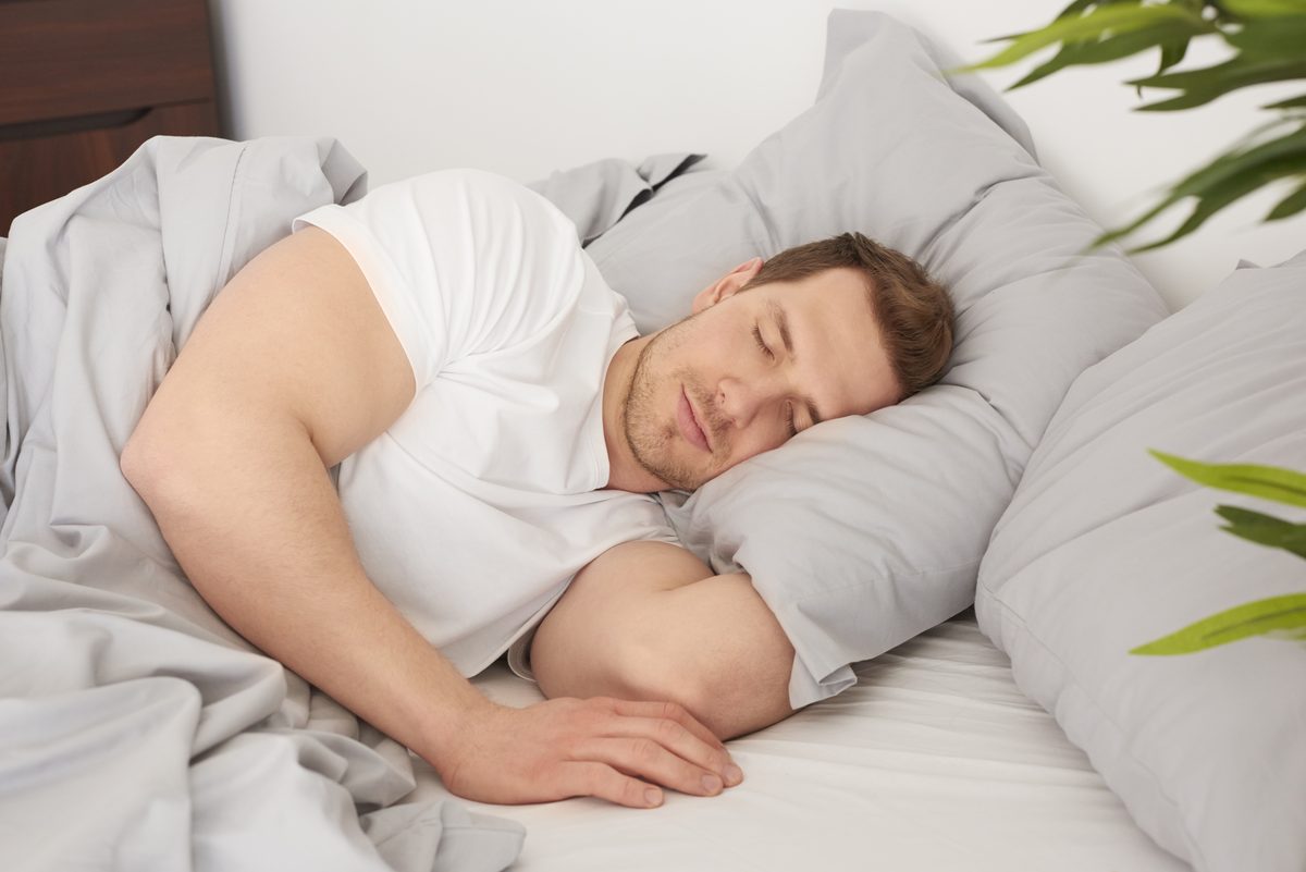 Homme endormi dans un lit aux draps gris