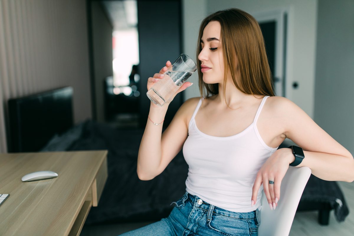 Young woman drinking a glass of water, sitting at home