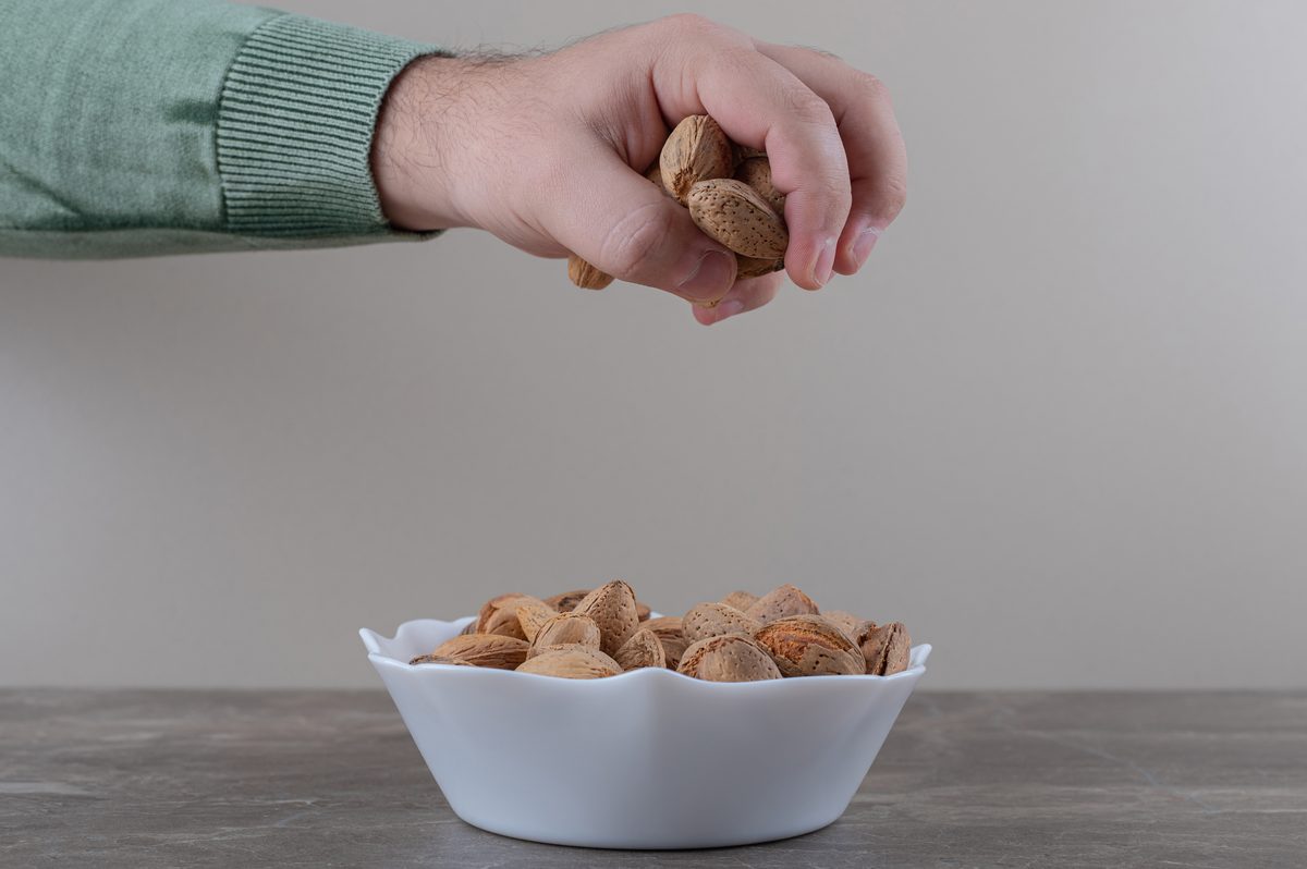 Main qui dépose des amandes en coque dans un bol blanc