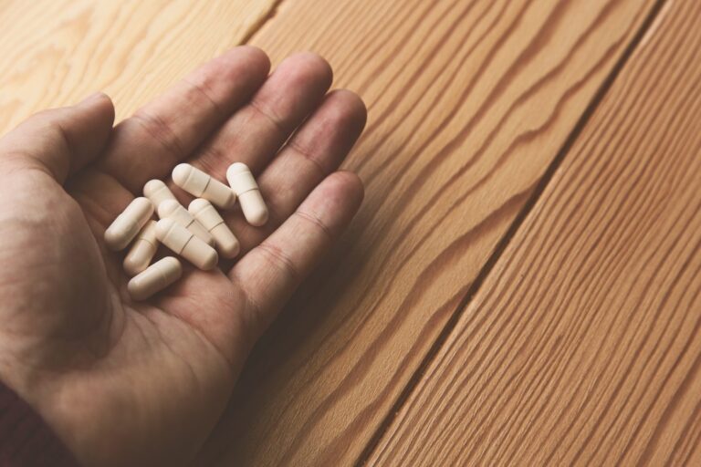 Hand holding a handful of white capsules above a wooden table