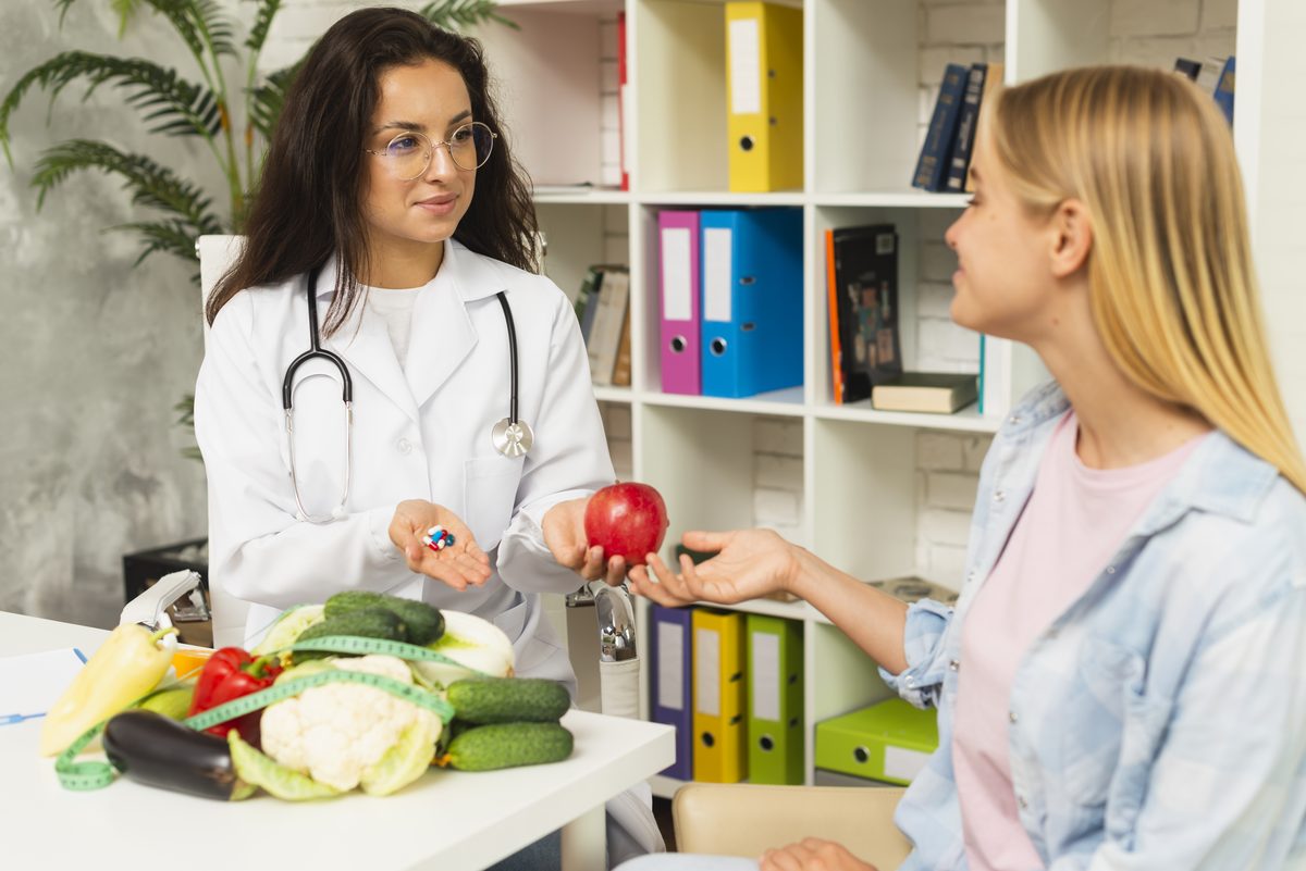 Médecin en blouse tendant une pomme à une patiente, légumes sur le bureau