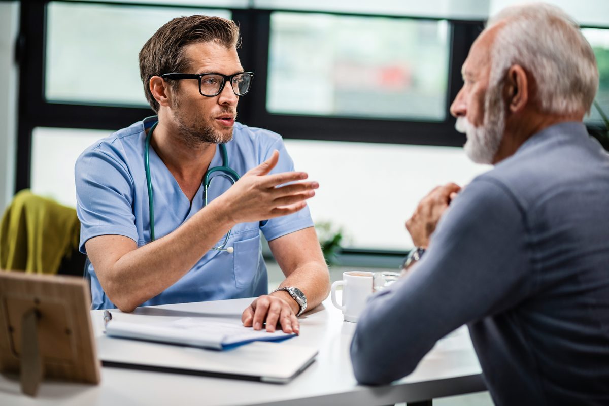 Médecin en tenue bleue qui échange avec un patient âgé en consultation
