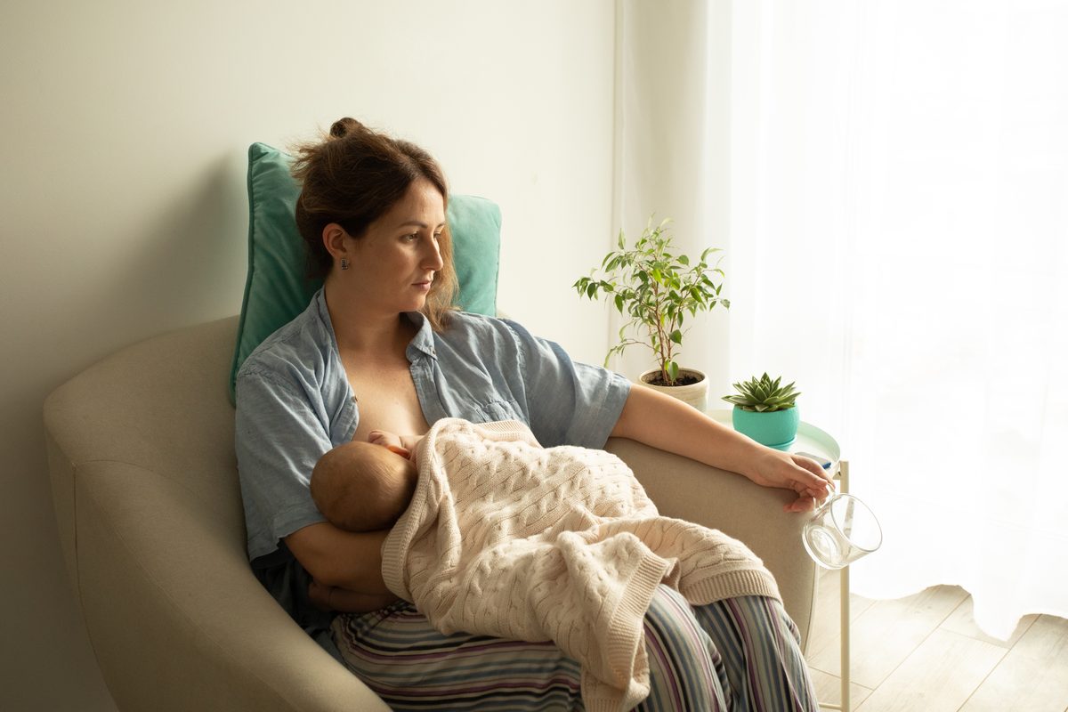 Mother breastfeeding her newborn in an armchair near a window