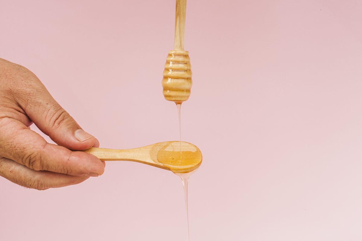 Honey running from a honey dipper into a wooden spoon held in the hand