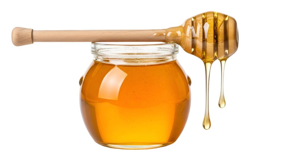 Golden honey dripping from a wooden spoon into a glass jar