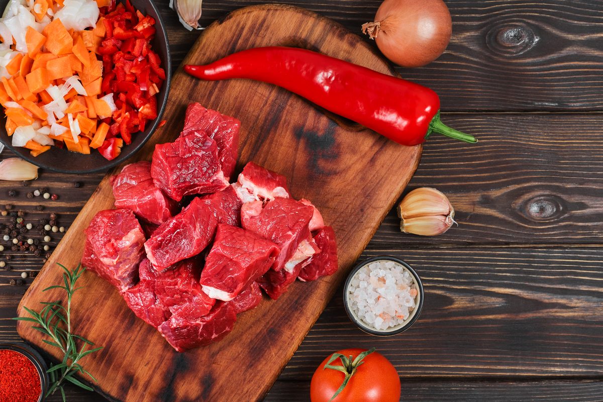 Pieces of raw beef, chilli and chopped vegetables on a wooden board