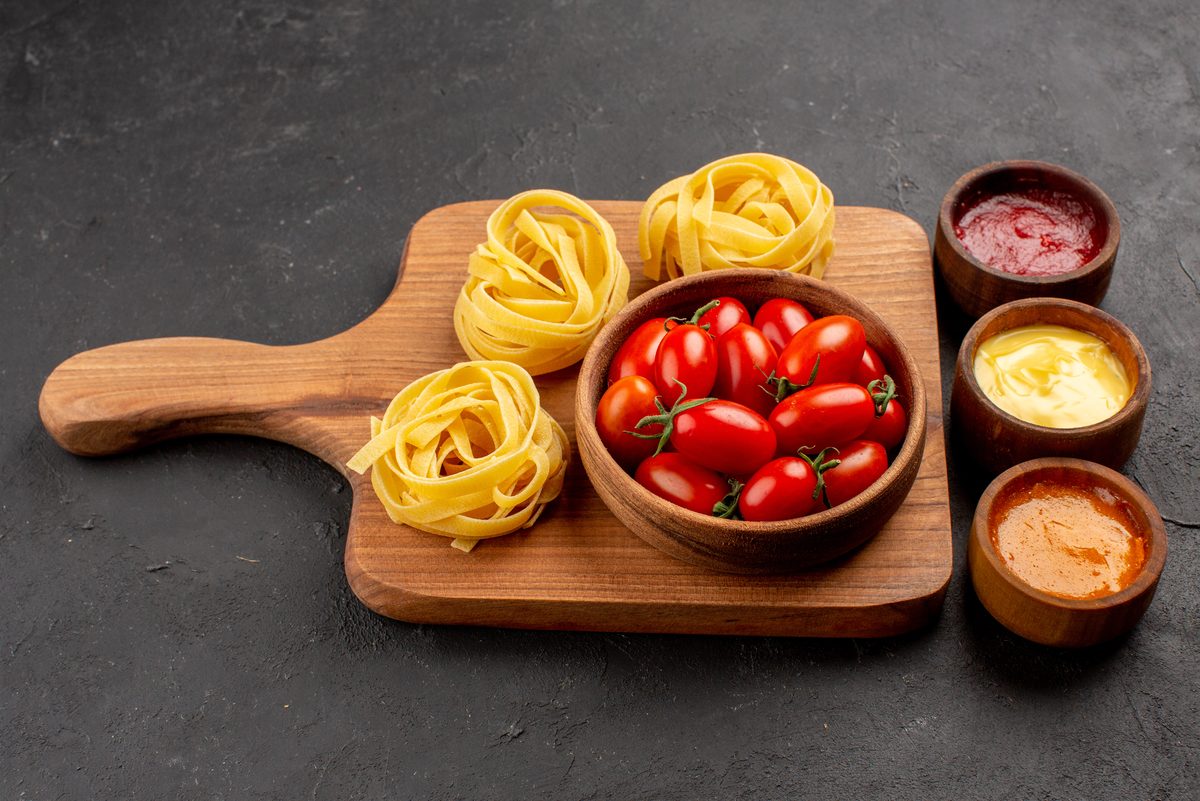 Nests of raw tagliatelle on a board with cherry tomatoes and sauces