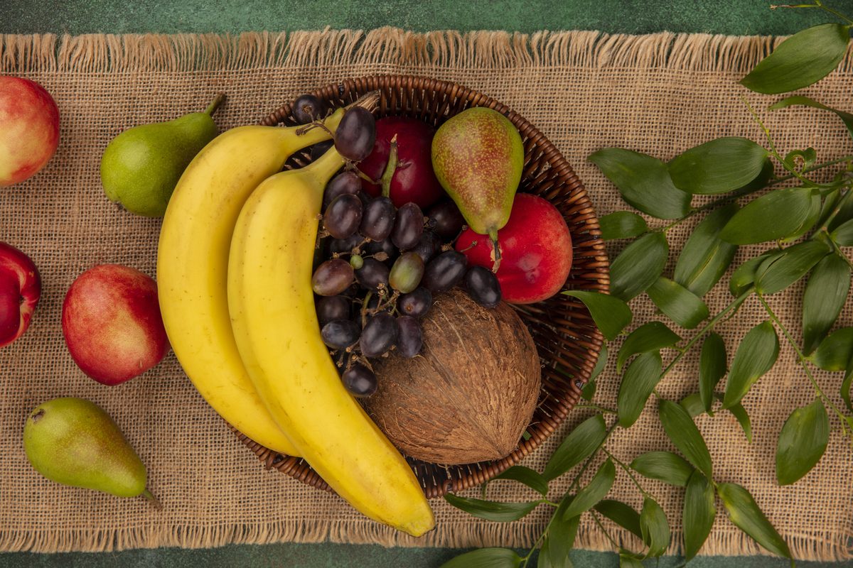 Basket of bananas, black grapes, pears, peaches and coconuts