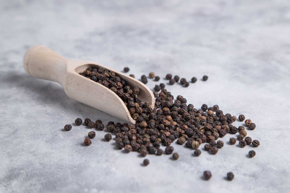 Wooden scoop and black peppercorns on a table